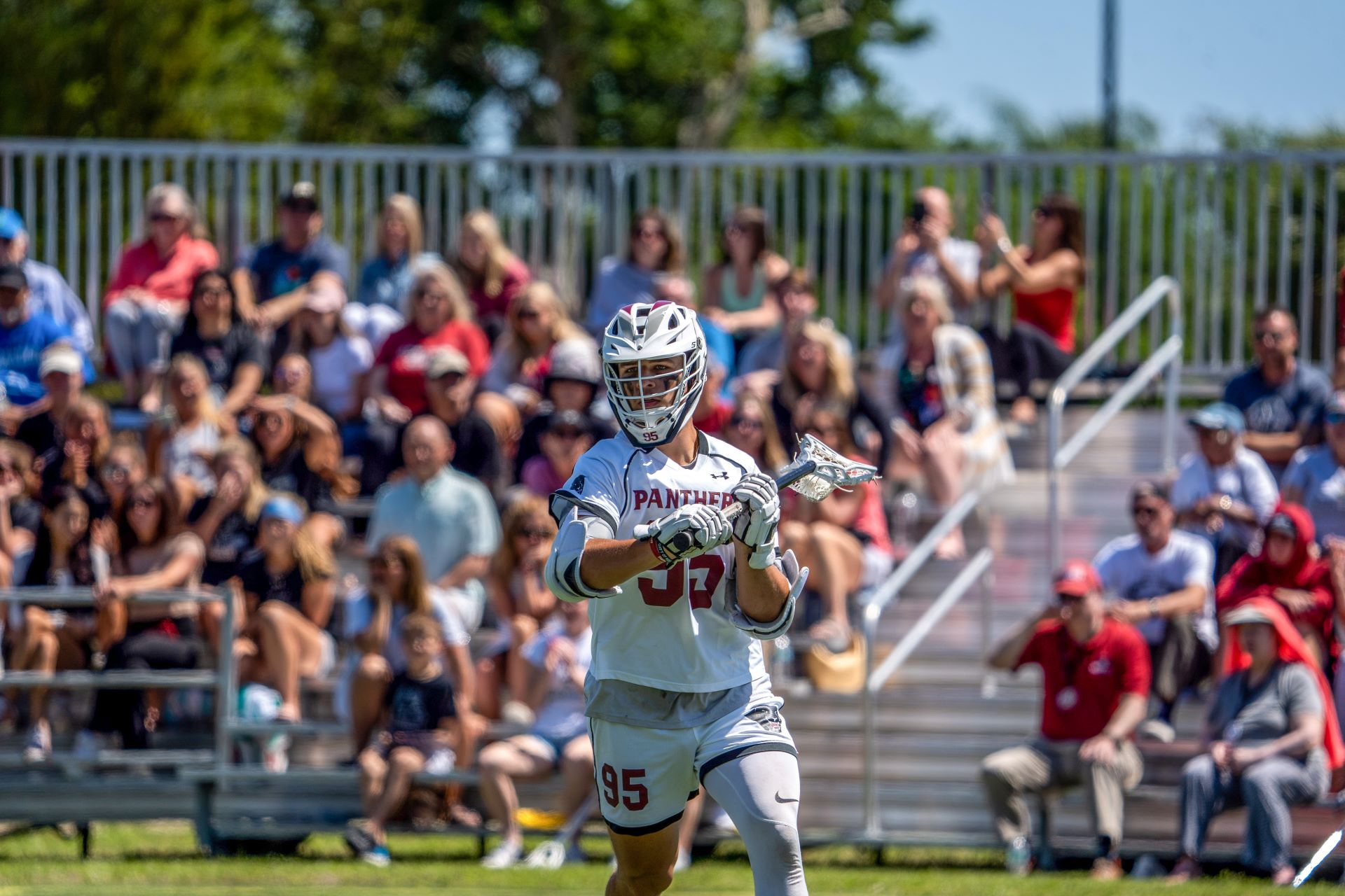 Florida Tech lacrosse player in action on the field, wearing number 95, with spectators watching from the bleachers in the background